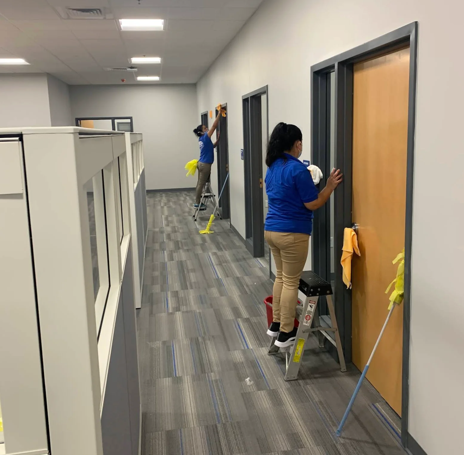 Cleaners detailing door frames along an office corridor