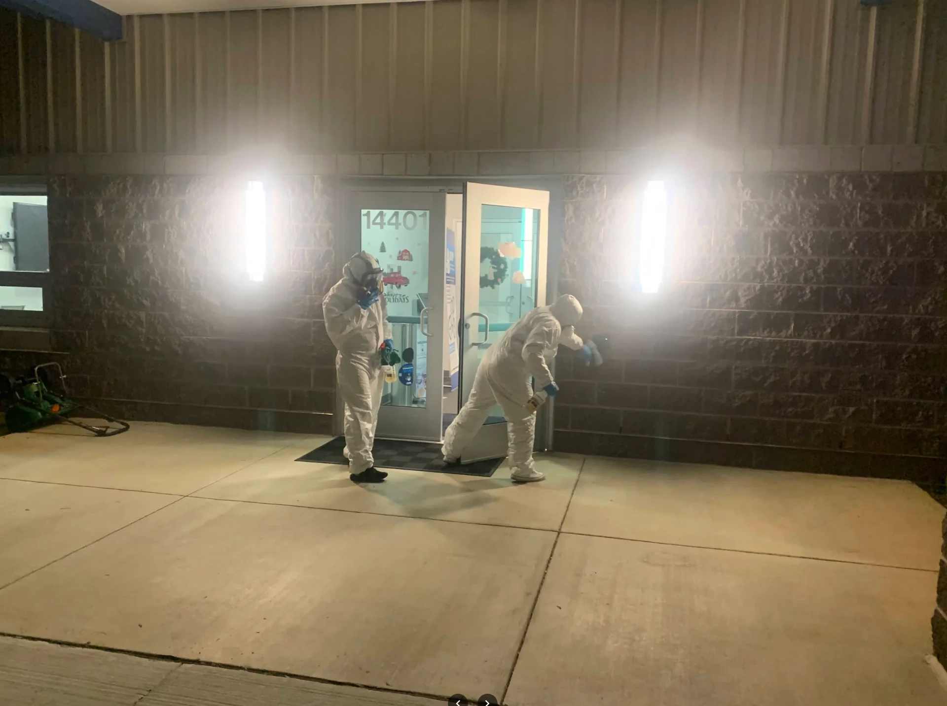 Crew in protective suits sanitizing a building entrance at night
