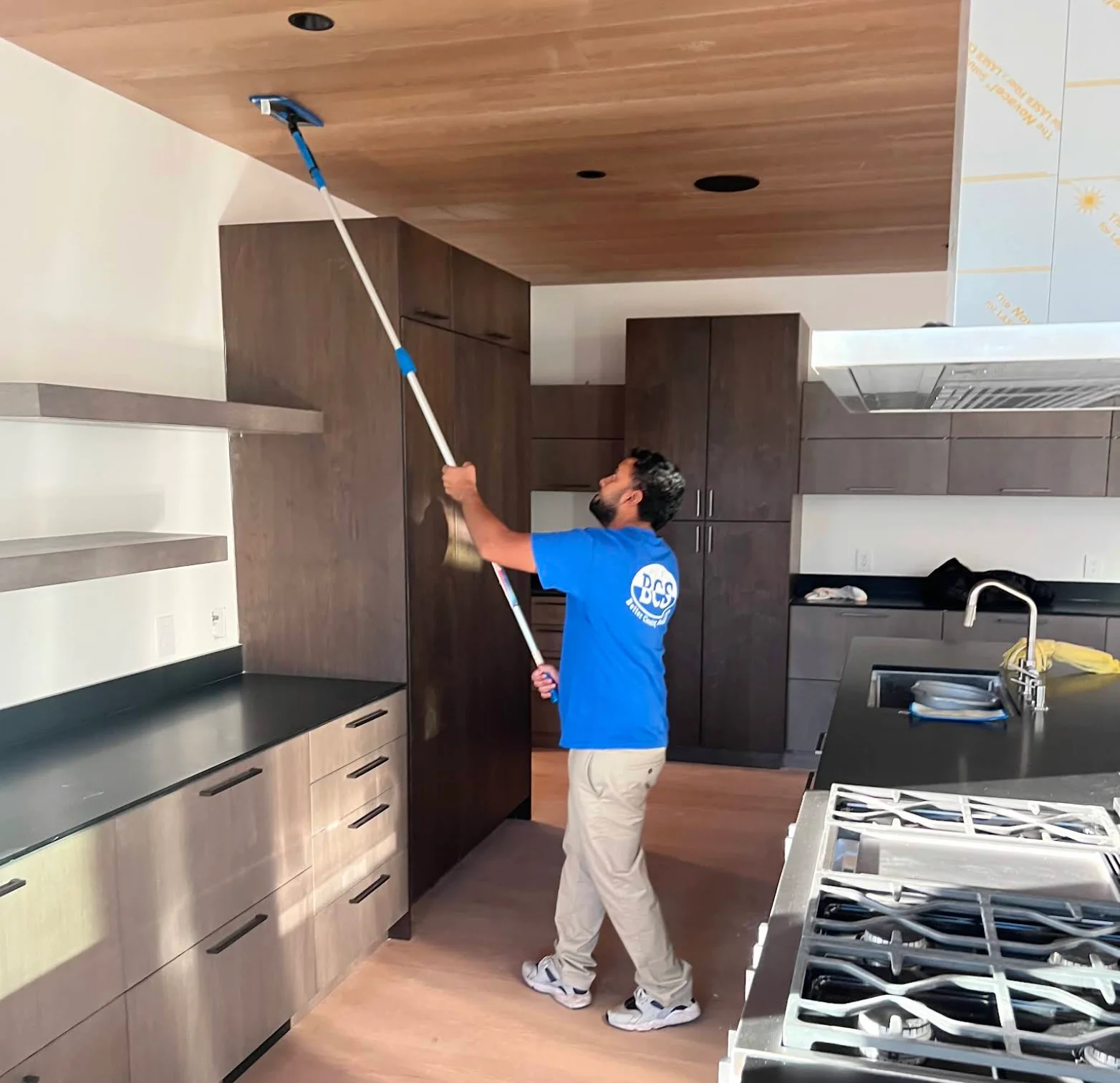 Technician dusting a high wood ceiling with an extension pole